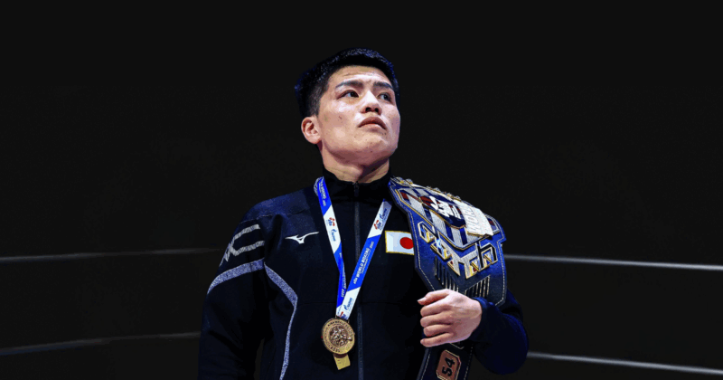 坪井智也選手が世界選手権で金メダルを獲得した際の表彰台での姿。日本代表のMIZUNO製黒色ジャージを着用し、胸に金メダルをかけ、世界チャンピオンベルトを右手で持って誇らしげに上を見つめている。