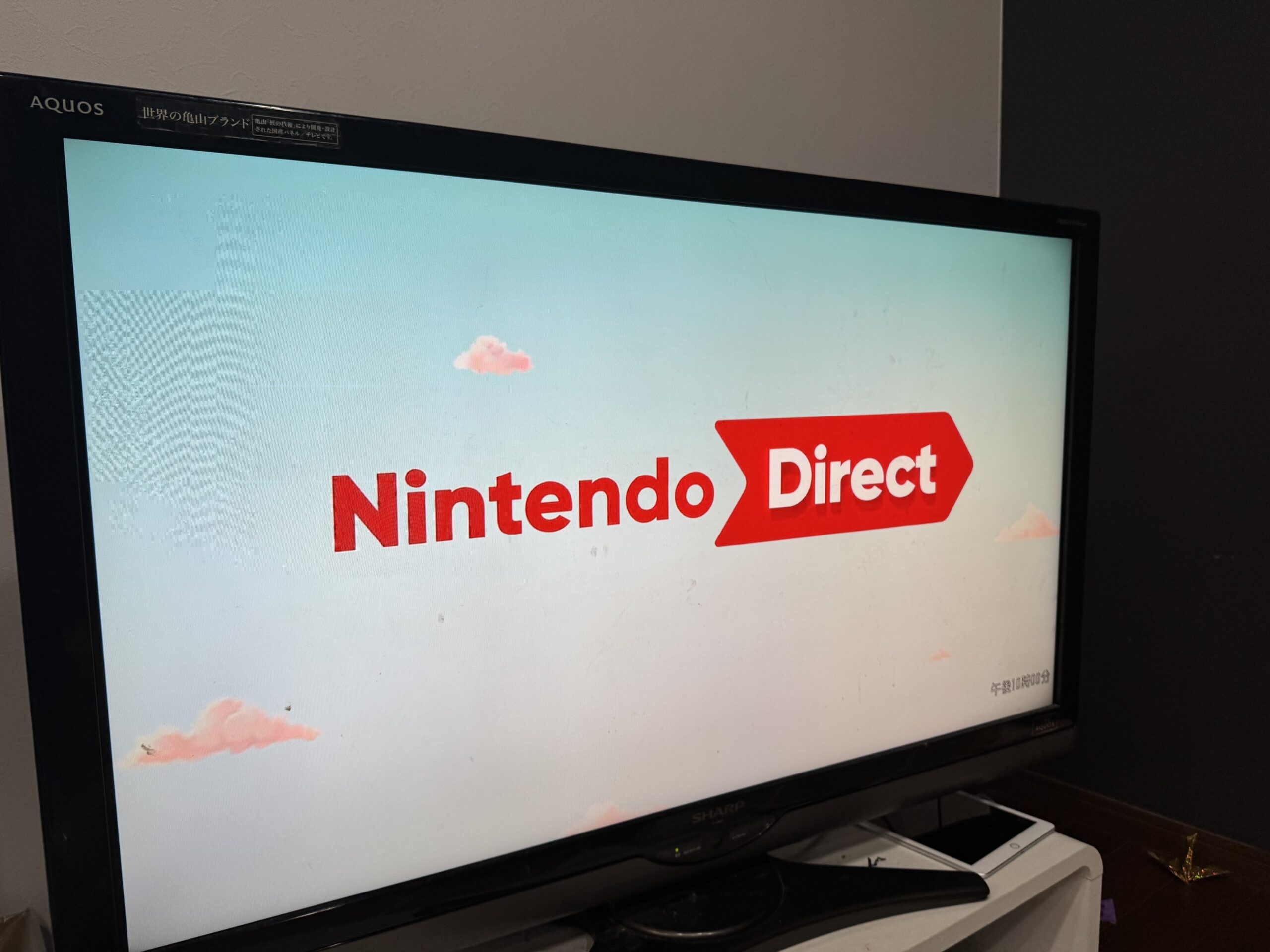Nintendo Directロゴが表示されているシャープAQUOSテレビの画面。水色の背景にピンクの雲が浮かび、中央に赤いNintendo Directのロゴが表示されている。