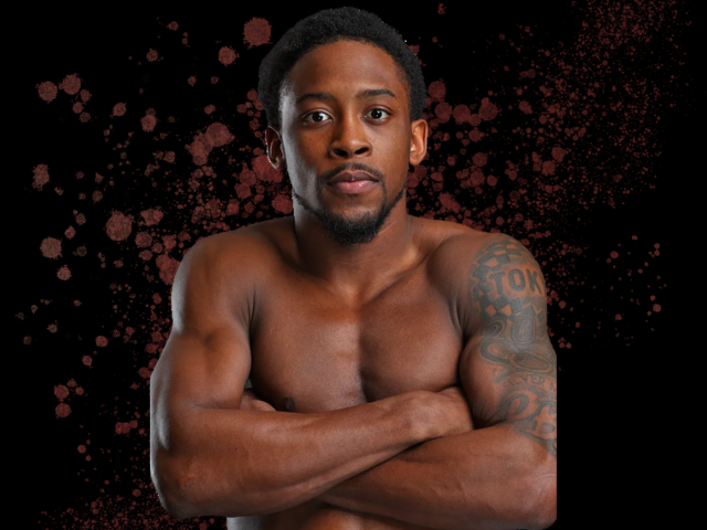 WBO世界ライト級王者キーショーン・デービスの上半身ポートレート写真。腕を組んでカメラに向かって真剣な表情をしており、右腕に入れ墨が見える。黒い背景に赤い飛沫模様が施されている。