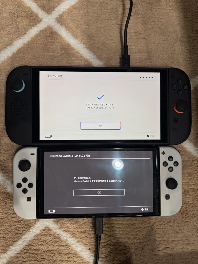 Nintendo Switch 2のデータ移行完了画面。上のSwitch 2には青いチェックマークと「まるごと転送が完了しました!」のメッセージ、下のSwitch有機ELには「データを送りました」の完了通知が表示されている